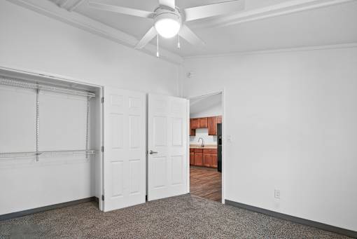 A room with a ceiling fan and a door leading to a kitchen.
