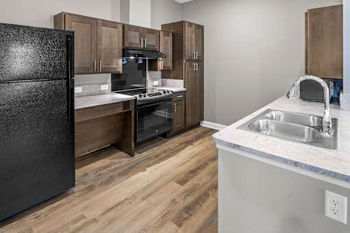 A kitchen with a black refrigerator, wooden cabinets, and a white countertop.