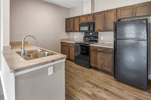 A kitchen with a black refrigerator, sink, and stove.