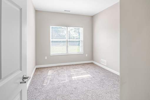 A room with a carpeted floor and a window with blinds.