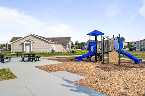 A playground with a blue slide and picnic tables.