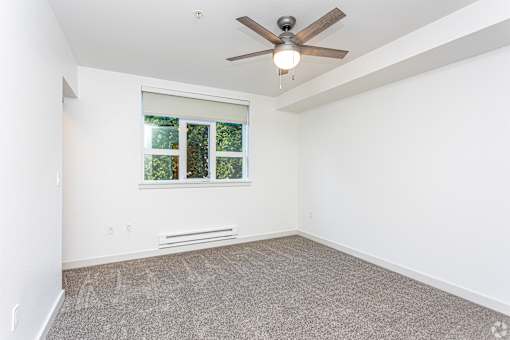 A room with a ceiling fan and a window with a view of trees.