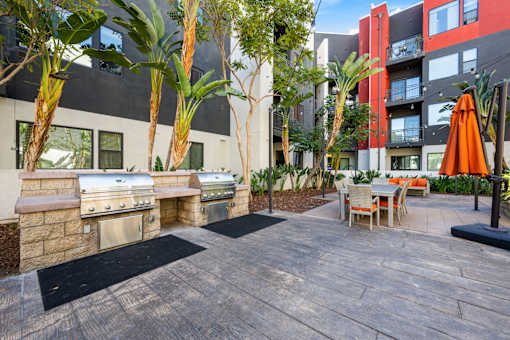 A patio with a grill and chairs is surrounded by trees.