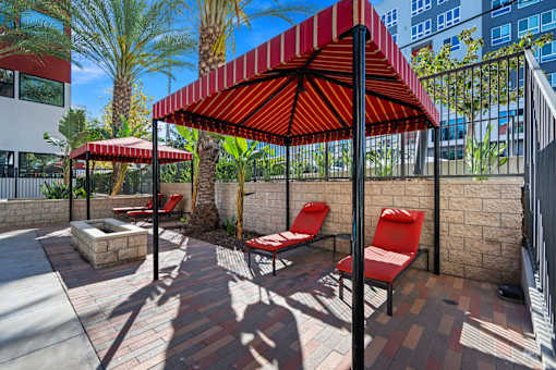 A red and white striped umbrella is over a table with two red chairs.