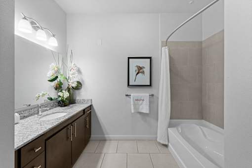 A bathroom with a white tub, sink, and a framed picture on the wall.