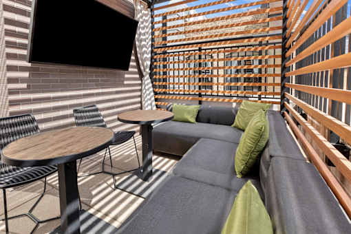 A patio with a black couch, a wooden table, and a TV mounted on the wall.
