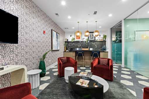 A modern waiting room with a black and white checkered floor, red chairs, and a bar area.