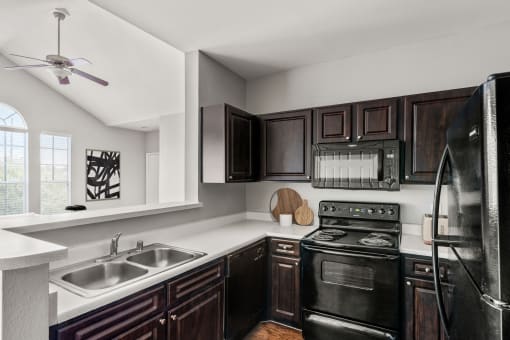 a kitchen with black appliances and white counters and dark wood cabinets at Veranda at Centerfield in Houston, Texas 77070