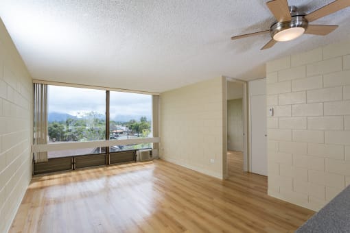 an empty living room with wood floors and a large window at Palms of Kilani Apartments, Wahiawa, HI, 96786