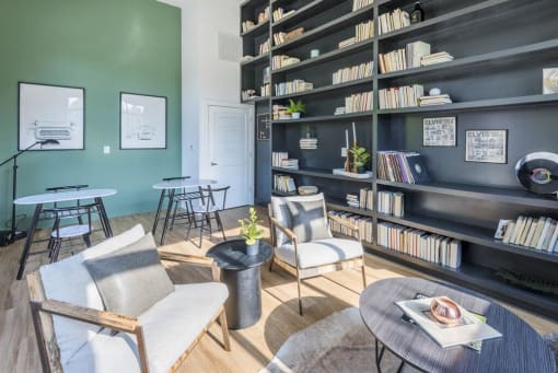 Resident library and coworking lounge with cozy chairs and tables surrounded by bookshelves at The Merchant Apartments, Charleston, South Carolina