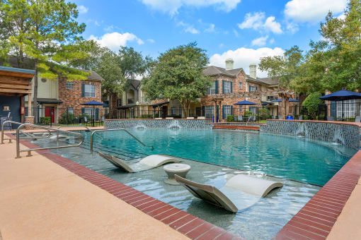 a swimming pool with two lounge chairs in front of a building at Aston at Cinco Ranch, Katy, 77450