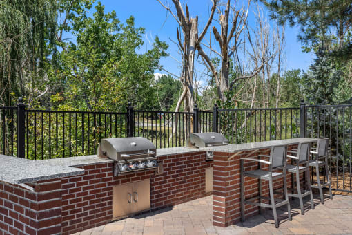 a brick outdoor kitchen with two bbqs and a table with chairs at Arcadia Apartments, Centennial
