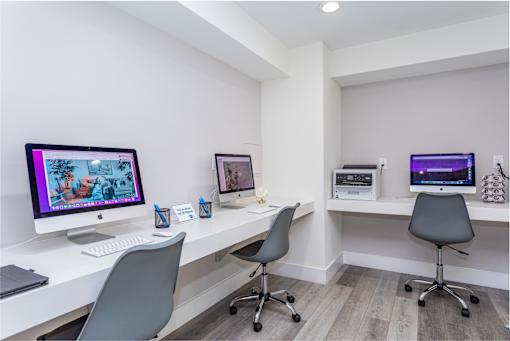 A white desk with a computer monitor and two chairs.