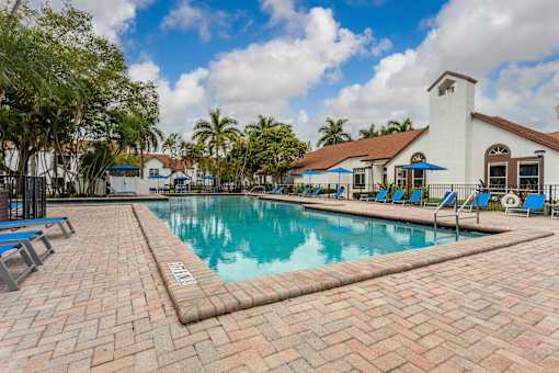 A pool with a brick walkway and a white building in the background.
