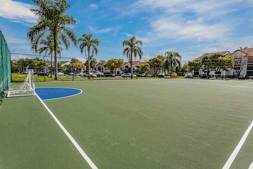 A tennis court surrounded by palm trees and residential buildings.