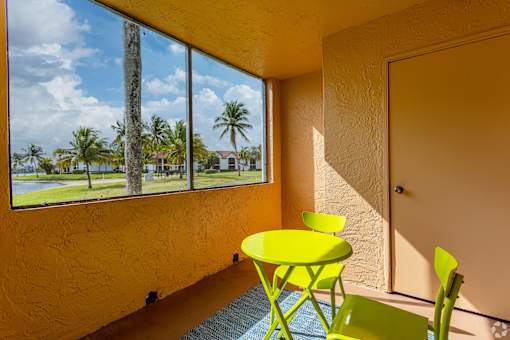 A yellow table and chairs are in front of a window with a view of a palm tree and a blue sky.