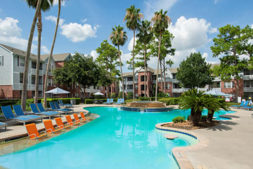 a large swimming pool with orange chairs in front of apartment buildings at Veranda at Centerfield, Texas