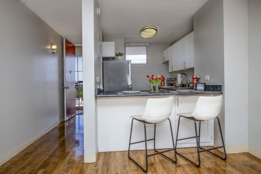 a kitchen with white cabinets and a counter with two white chairs at Waikele Towers Apartments, Waipahu, 96797