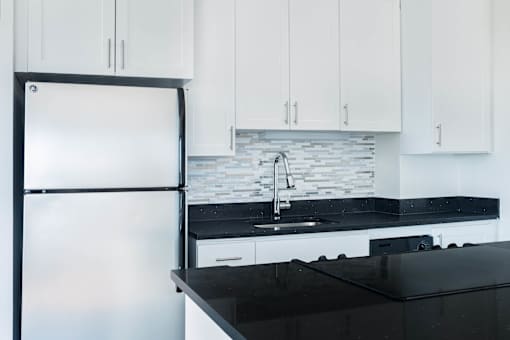 A modern kitchen with a black countertop and white cabinets at Skye at Belltown Apartments, Washington 98121