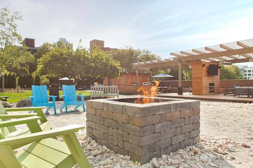A fire pit is in the middle of a gravel area with blue and green chairs around it at Skye at Belltown Apartments, Seattle, WA 98121