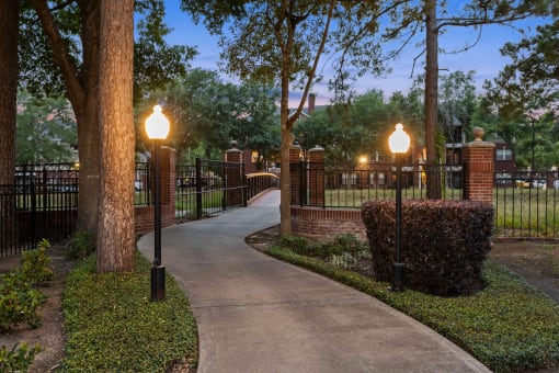 a walkway through a park with lamps and a fence at Villages of Cypress Creek, Texas, 77070