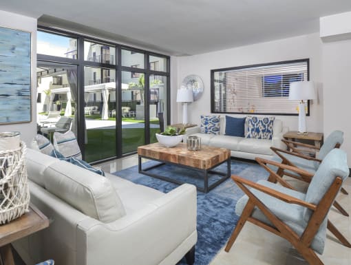 a living room with white couches and chairs and large windows at District West Gables, West Miami, Florida 33155