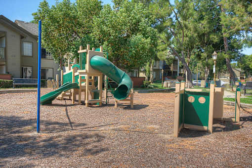 A playground with a green slide and a wooden structure.