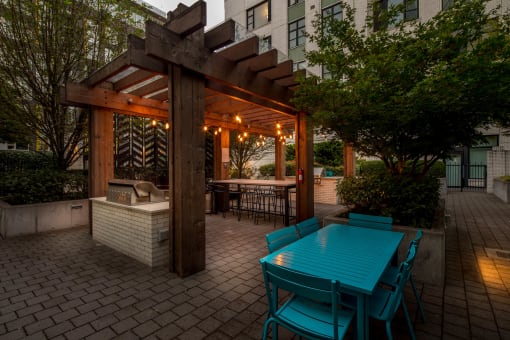 a wooden pergola with a turquoise table and chairs on a brick patio at The Parker Apartments, Portland, OR, 97209
