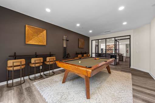 A pool table is surrounded by four chairs in a room with a brown wall and a painting.