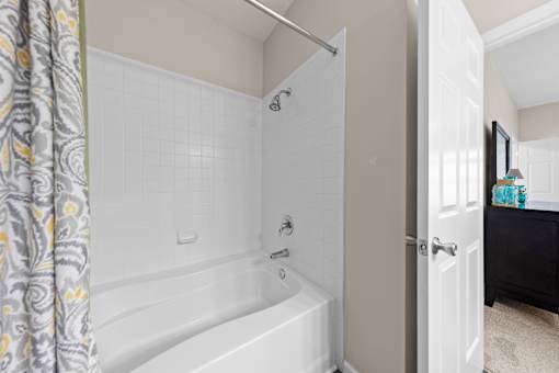 A white bathtub with a shower head and a shower curtain.