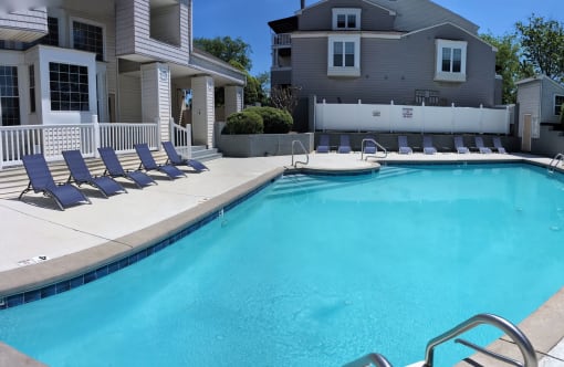 a swimming pool with blue chairs next to a house