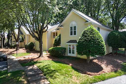 A yellow house with a white door and windows surrounded by green trees.