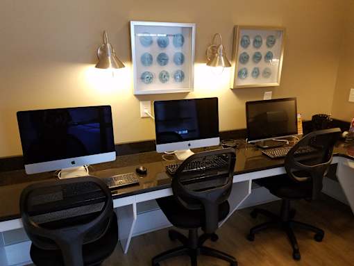 A computer desk with four chairs and two monitors.