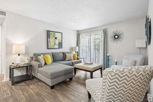 A living room with a grey couch, a grey armchair, and a small table with a lamp on it.