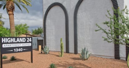A sign for Highland 24 Apartment Home is in front of a white building.