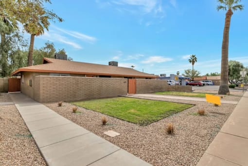 the front yard of a brick house with a lawn and a sidewalk