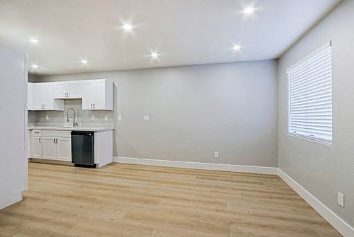 an empty living room with a kitchen with white cabinets and a window