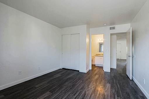 A room with white walls and wood flooring with a doorway leading to another room.
