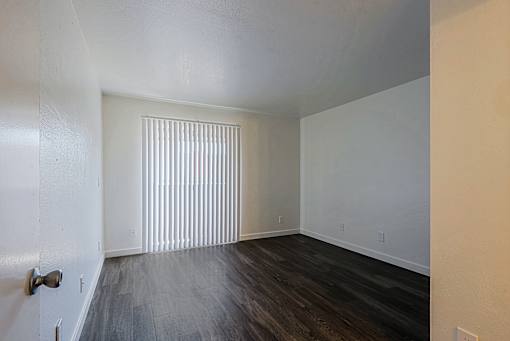 A room with a wooden floor and a window with blinds.
