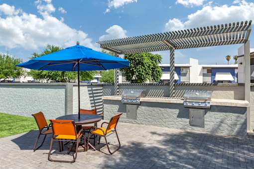 A blue umbrella is on a patio table with chairs.