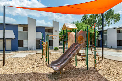 A playground with a yellow slide and a blue building in the background.
