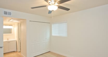 A room with a ceiling fan and a window with blinds.