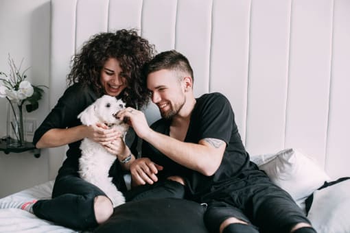 a man and a woman sitting on a bed holding a white dog