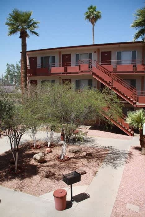 A red mailbox sits on a sidewalk in front of a building with a red staircase at Ambassador West Apartments, Phoenix, AZ