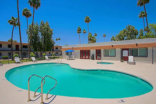 A large swimming pool surrounded by palm trees and lounge chairs at Aspire Mesa, Mesa.