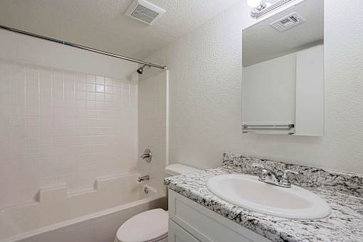 A white bathroom with a marble counter top and a white toilet.