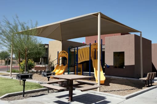A playground with a yellow slide and a brown picnic table.