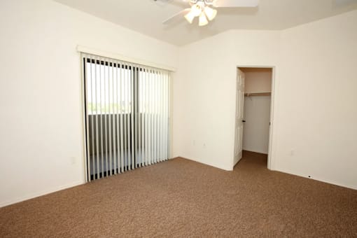 A room with a carpeted floor, a ceiling fan, and a window with blinds.