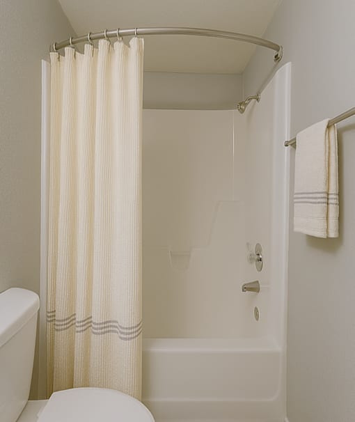 A white bathroom with a toilet, a shower with a curtain, and a towel hanging on the wall at Connect on Northern, Glendale, AZ 85301