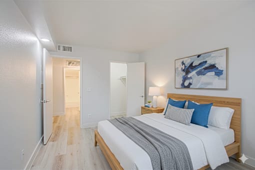 A bedroom with a bed, nightstand, and a painting on the wall.